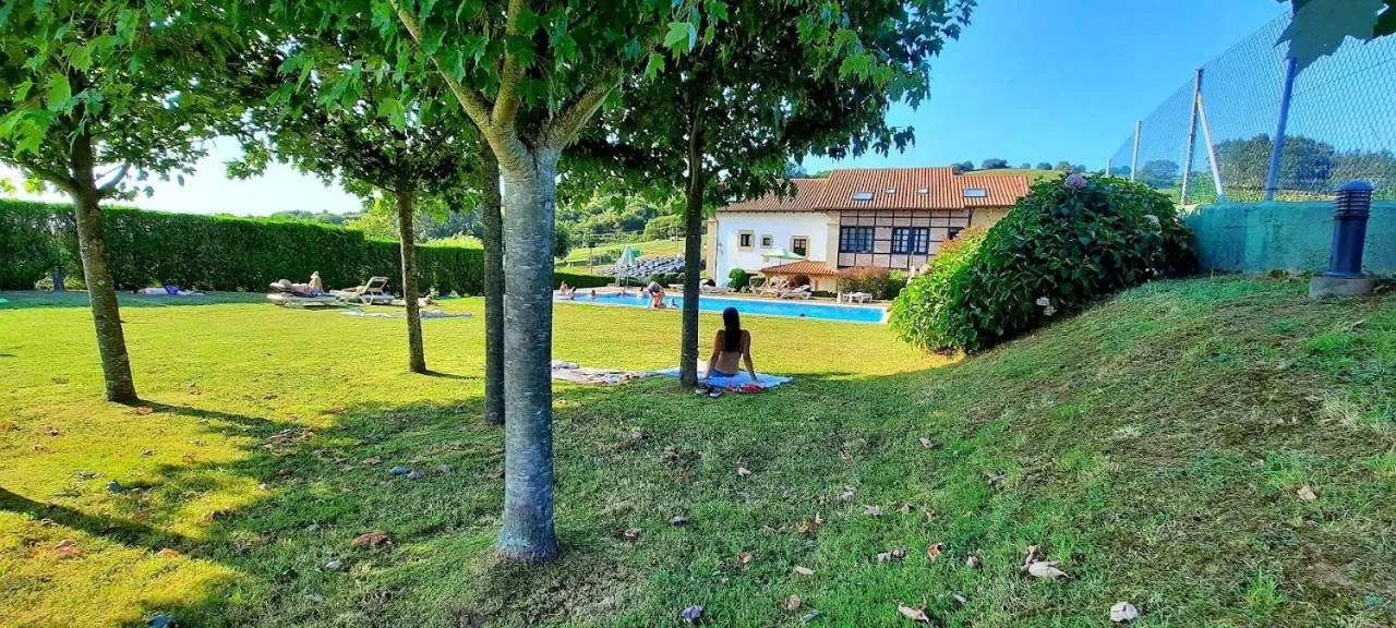 Une personne est assise sur une pelouse verte devant une piscine et un bâtiment.