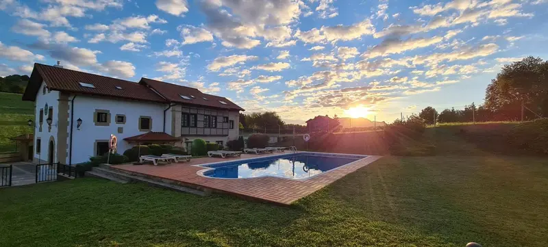 Bâtiment blanc et rouge avec piscine ensoleillée et ciel nuageux.