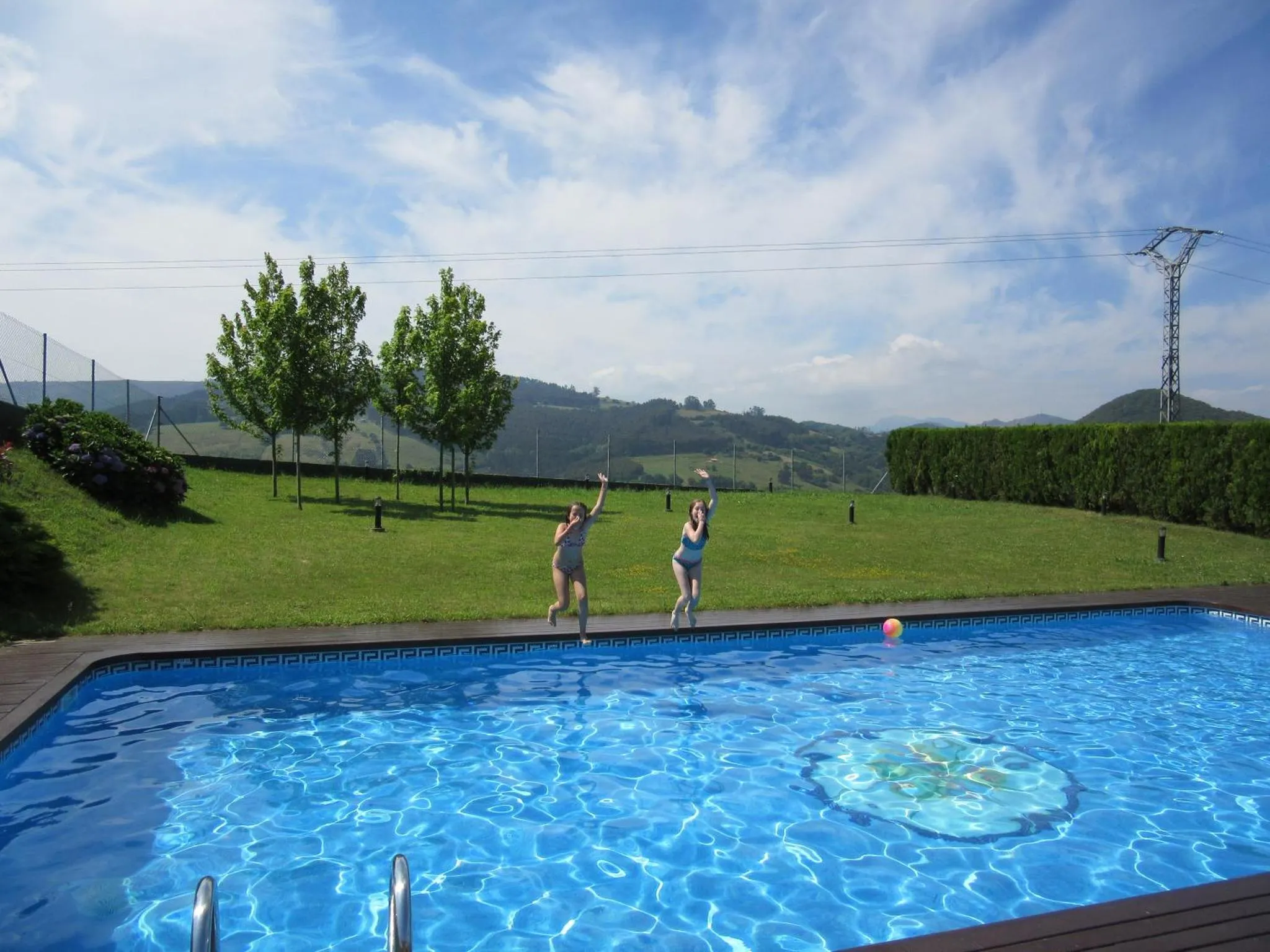 Deux personnes sautent dans une piscine ensoleillée avec vue sur un paysage verdoyant.