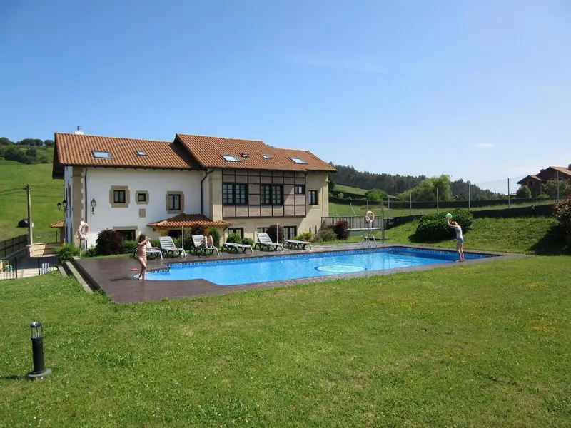 Une piscine rectangulaire bordée de transats se trouve devant un bâtiment à l'architecture traditionnelle.