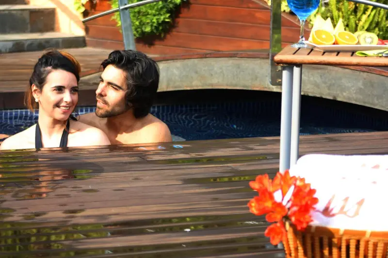 Un couple se détend dans une piscine ensoleillée, avec des boissons et des fleurs à proximité.