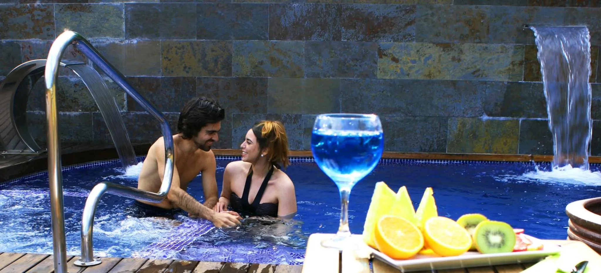Un couple se détend dans une piscine avec des fruits et une boisson.