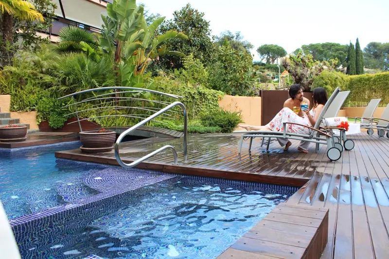 Deux personnes se détendent au bord d'une piscine ensoleillée, entourée de végétation luxuriante.