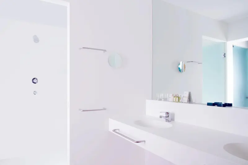 Une salle de bain minimaliste avec un grand miroir et un lavabo blanc.