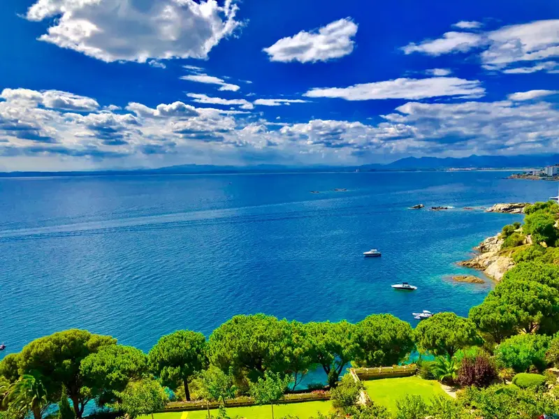 Vue aérienne sur une côte rocheuse et une mer bleue sous un ciel nuageux.