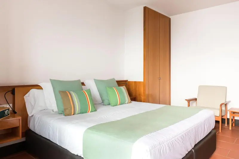 Une chambre lumineuse avec un grand lit recouvert d'une courtepointe verte et de coussins colorés.
