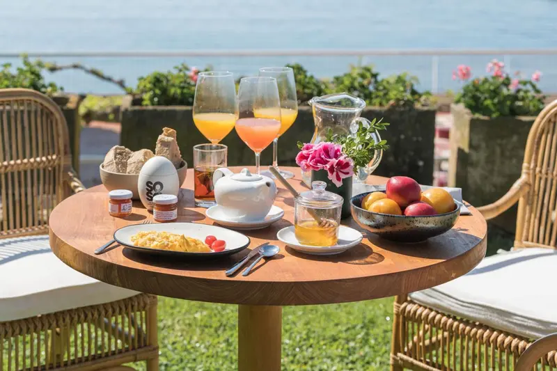 Une table ronde en bois est dressée pour le petit-déjeuner avec des boissons, des viennoiseries et des fruits.