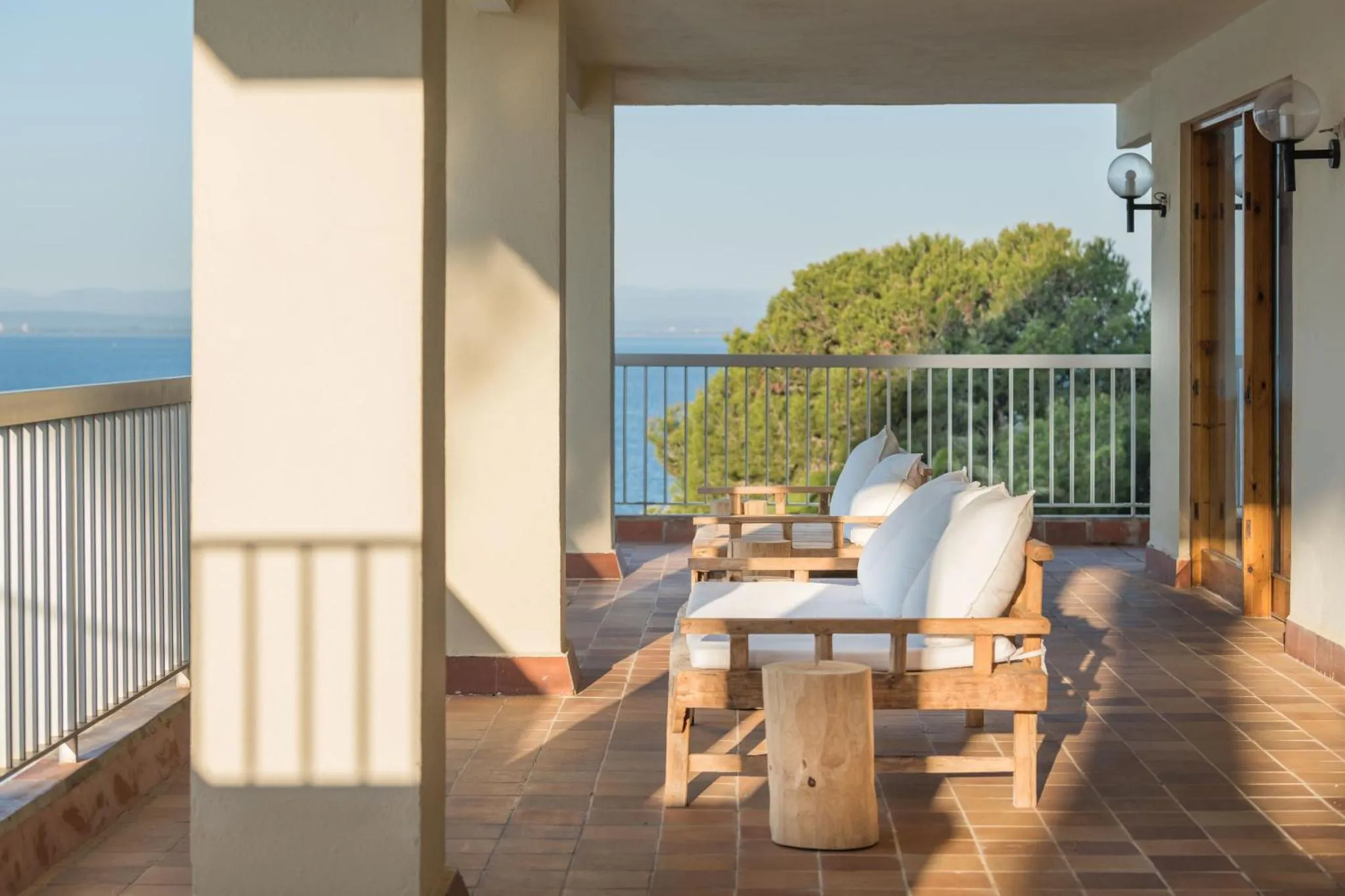 Terrasse ombragée avec canapé en bois et vue sur la mer.