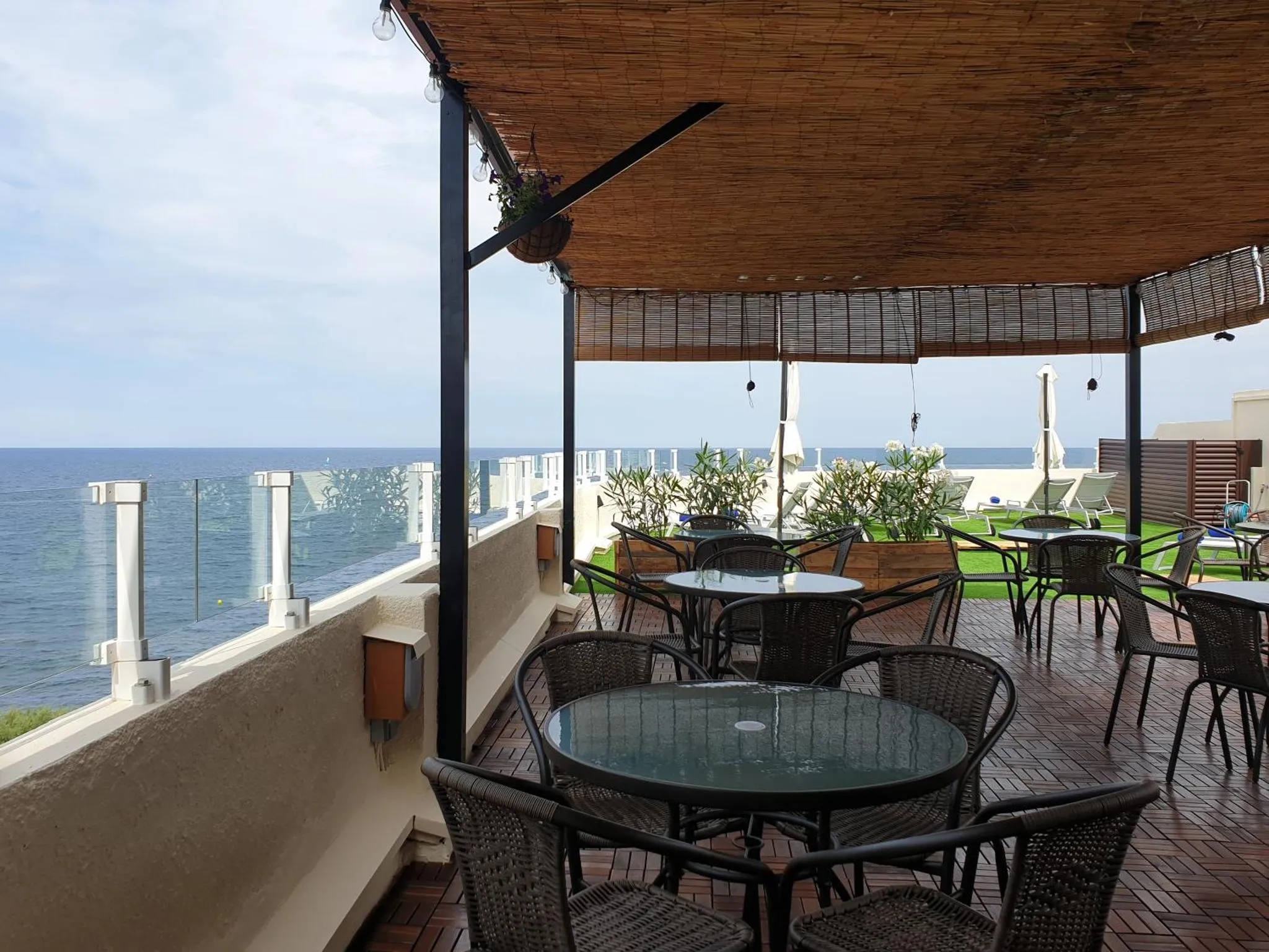 Terrasse ombragée avec tables et chaises donnant sur la mer.