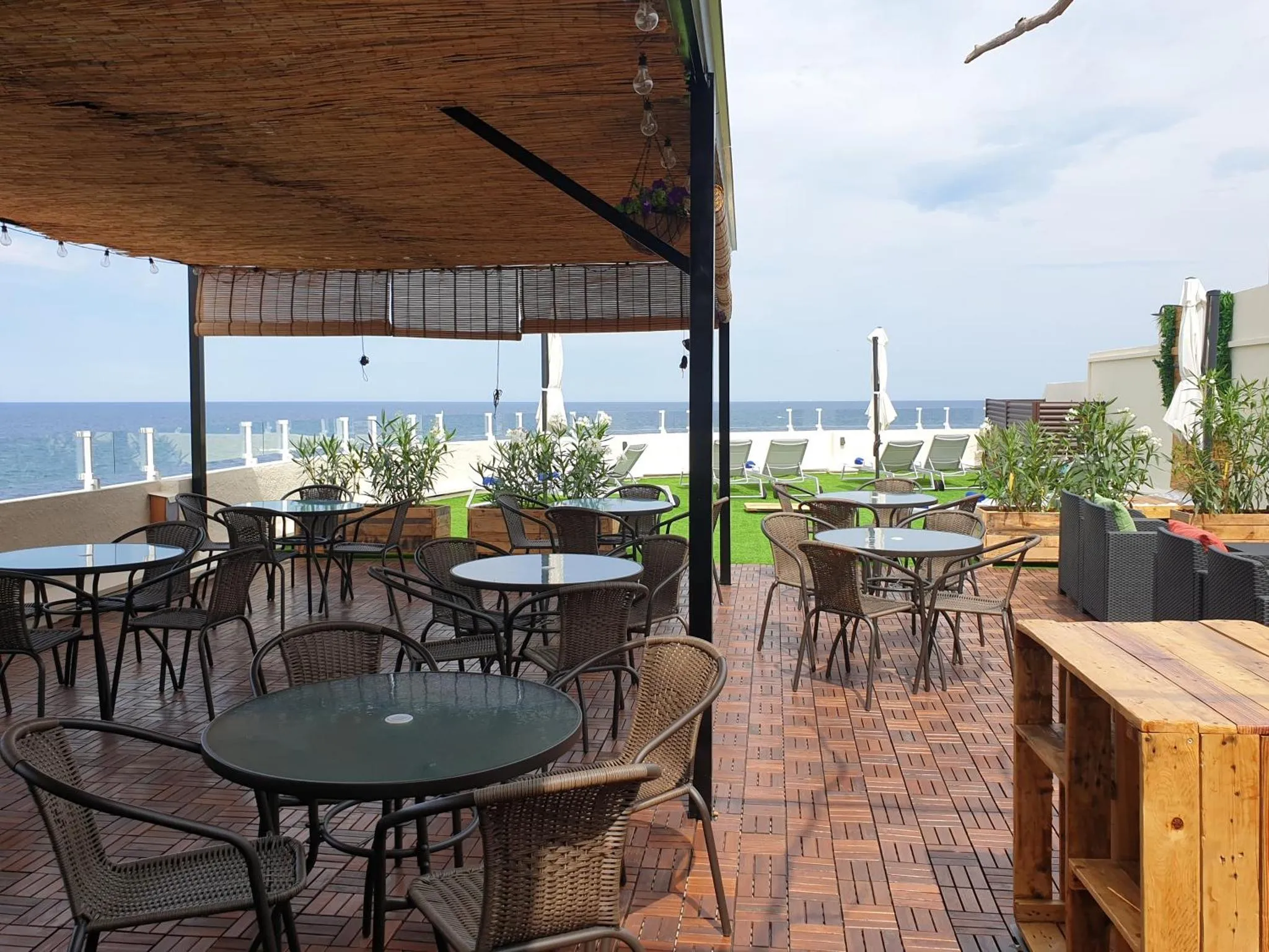 Terrasse ombragée avec tables et chaises en osier donnant sur la mer.