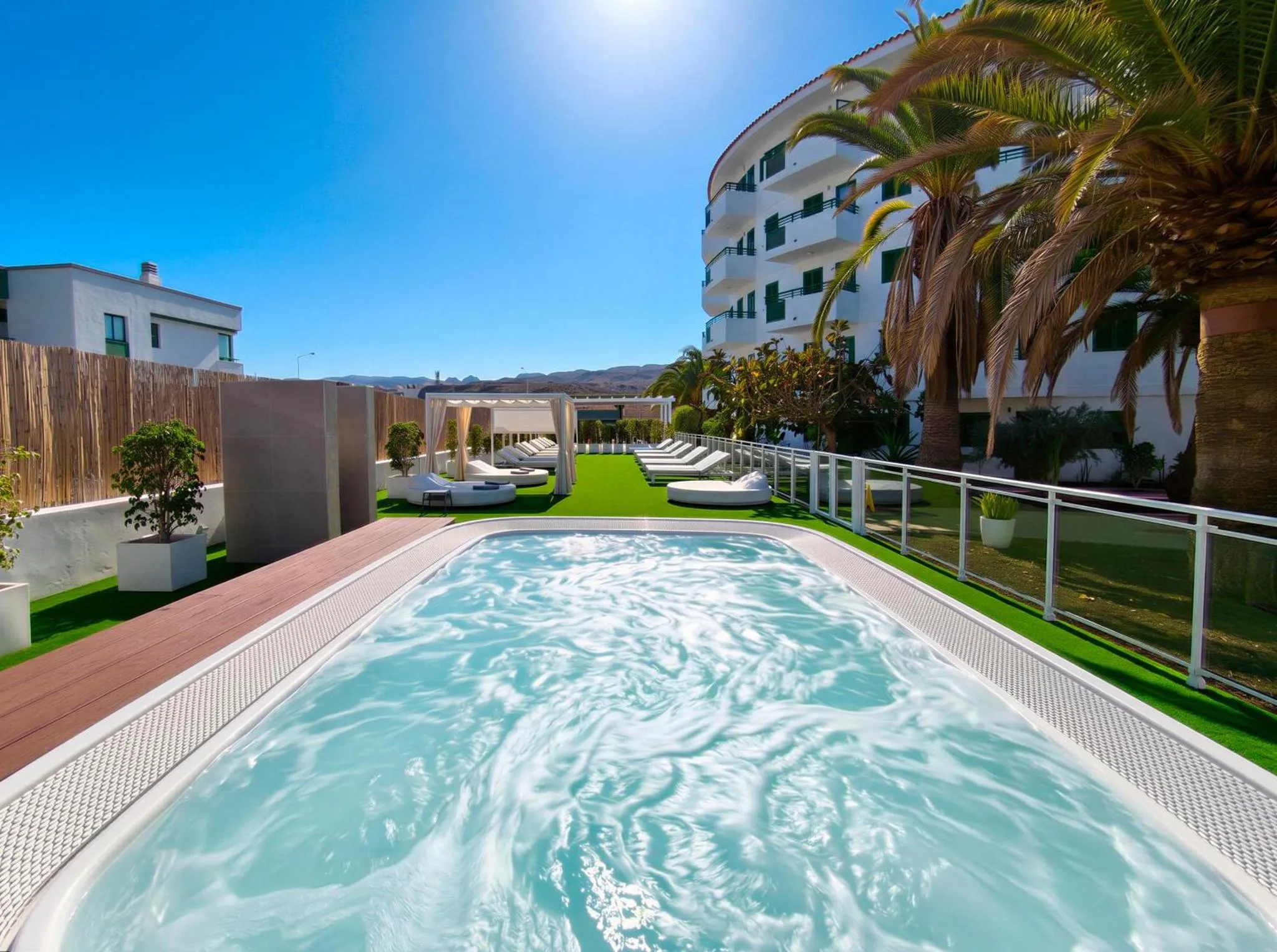 Une piscine turquoise avec des transats blancs et des palmiers en arrière-plan.