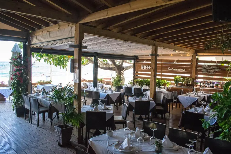 Une salle à manger extérieure avec des tables dressées en bord de mer.
