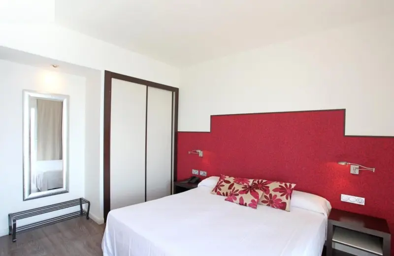 Une chambre lumineuse avec un grand lit et un mur rouge décoratif.