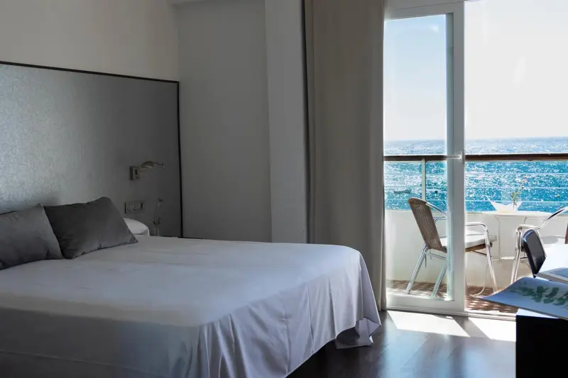 Une chambre lumineuse avec un grand lit et un balcon offrant une vue sur la ville.