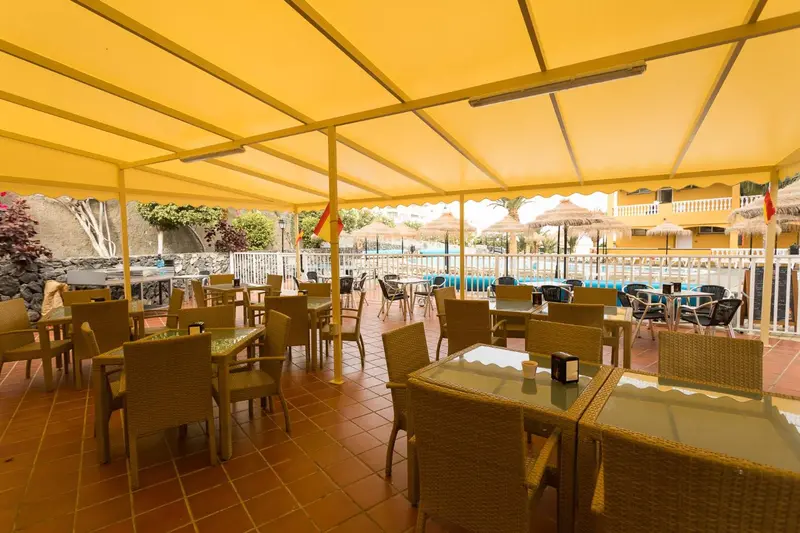 Terrasse ombragée avec tables et chaises disposées sur un sol carrelé.
