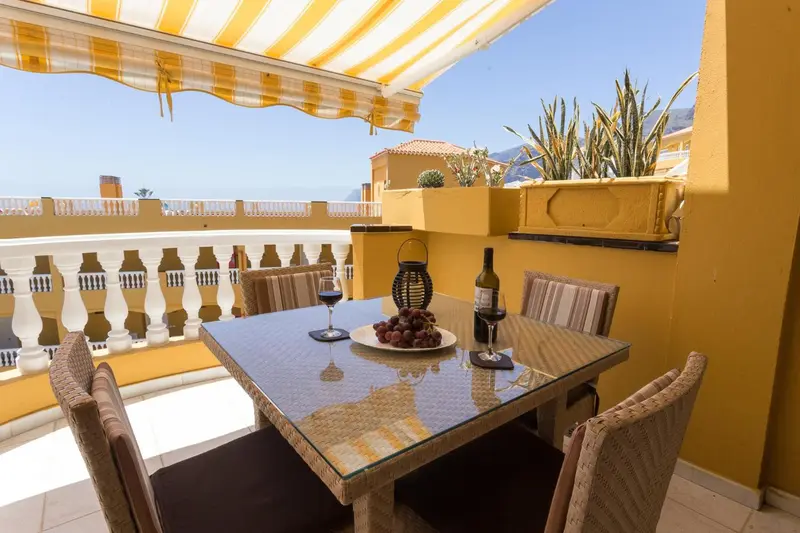 Une table avec des boissons et des fruits est mise en scène sur une terrasse ensoleillée.