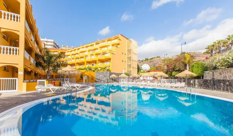 Piscine d'hôtel avec transats et bâtiments jaunes en arrière-plan.