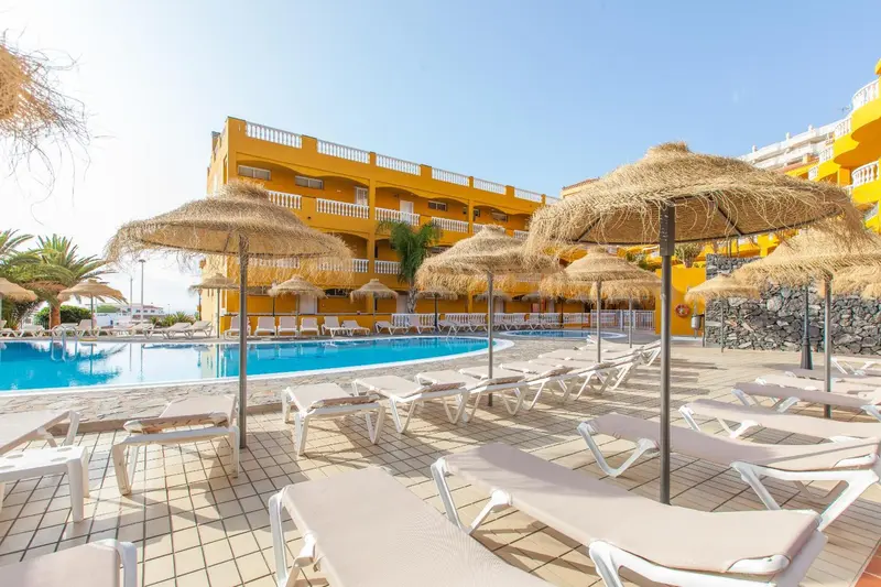 Transats et parasols ombragent une piscine turquoise dans un complexe hôtelier jaune.
