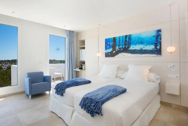Chambre lumineuse avec un grand lit et un fauteuil bleu.