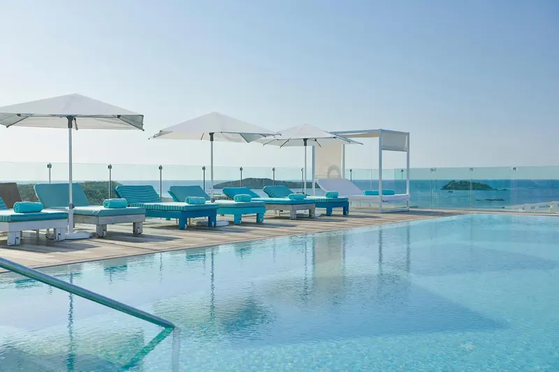 Transats bleus alignés au bord d'une piscine à débordement avec vue sur la mer.