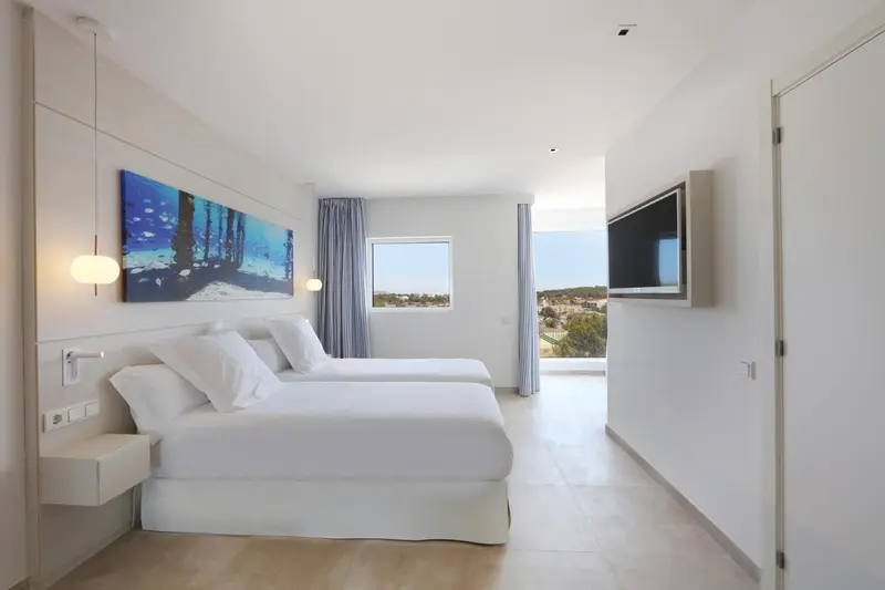 Chambre lumineuse avec un grand lit et une vue sur l'extérieur.