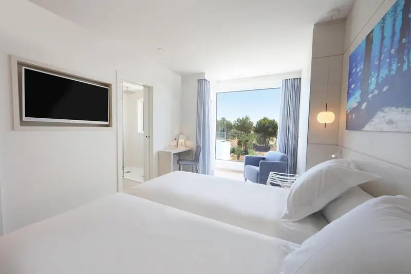 Une chambre lumineuse avec un lit blanc et un accès à un balcon.