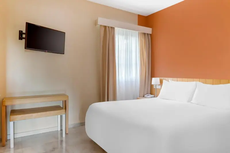 Une chambre lumineuse avec un lit blanc et un mur orange.