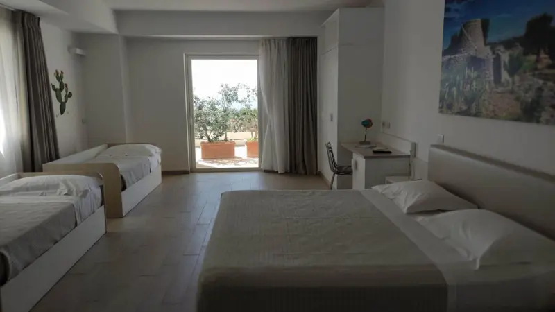 Chambre lumineuse avec deux lits simples et un lit double, donnant sur une terrasse.