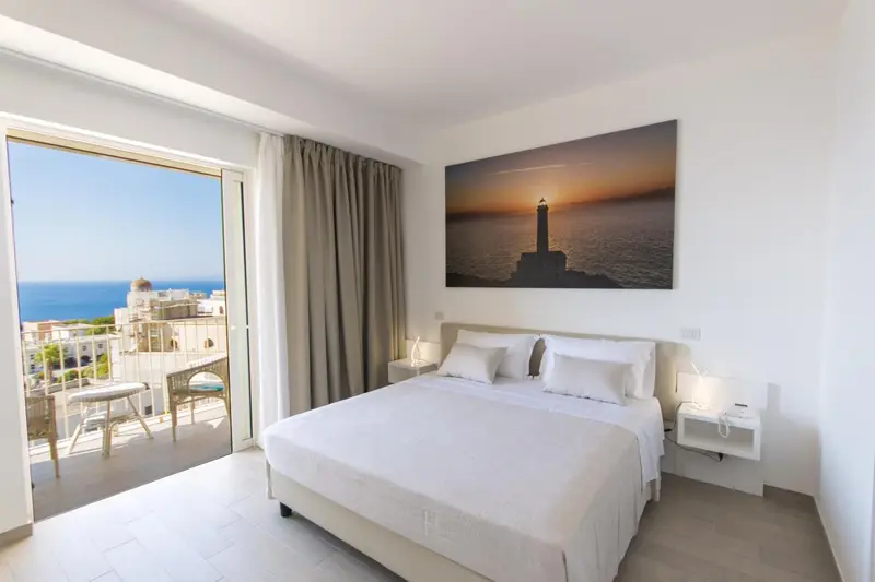 Chambre lumineuse avec un grand lit et une vue sur la mer depuis un balcon.
