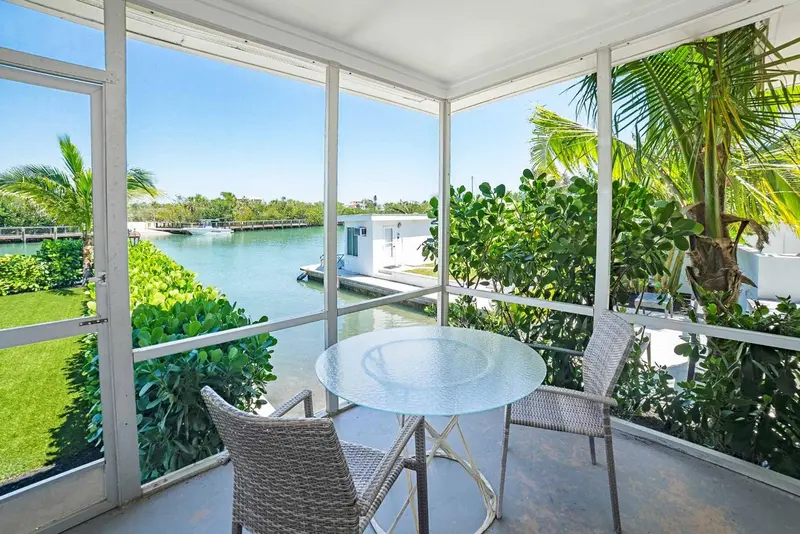 Terrasse avec table et chaises donnant sur un canal et une végétation tropicale.