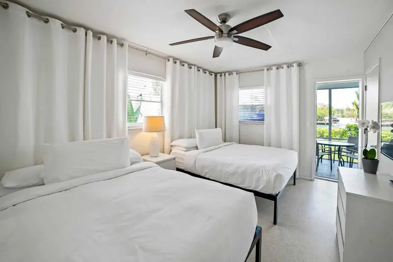 Une chambre lumineuse avec deux lits simples et une porte-fenêtre ouverte sur l'extérieur.