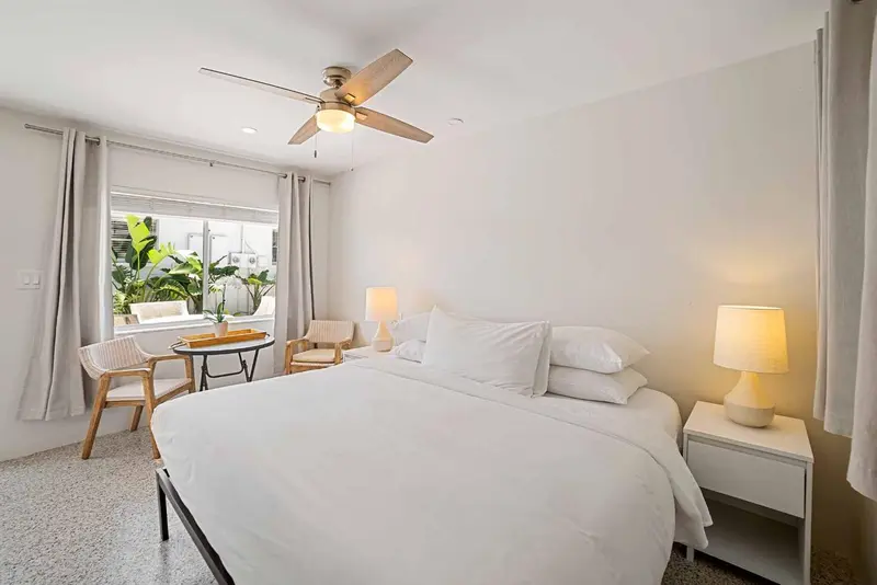 Une chambre lumineuse avec un lit fait et un coin salon près de la fenêtre.