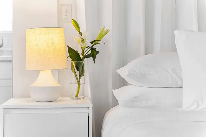 Une lampe de chevet illumine un lit aux draps blancs.