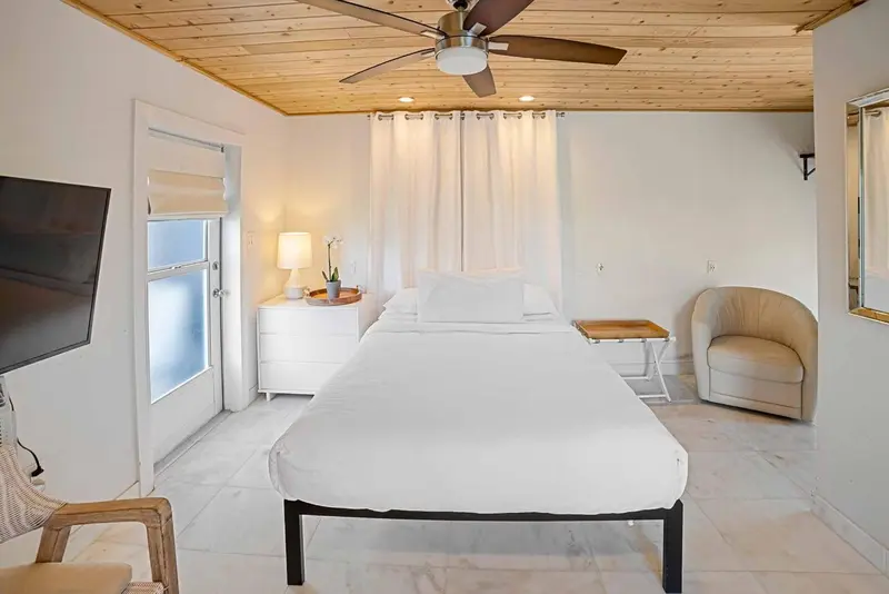 Une chambre lumineuse avec un lit blanc et un ventilateur de plafond.