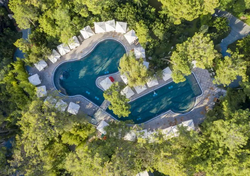 Vue aérienne d'une piscine sinueuse entourée de bungalows et de végétation luxuriante.