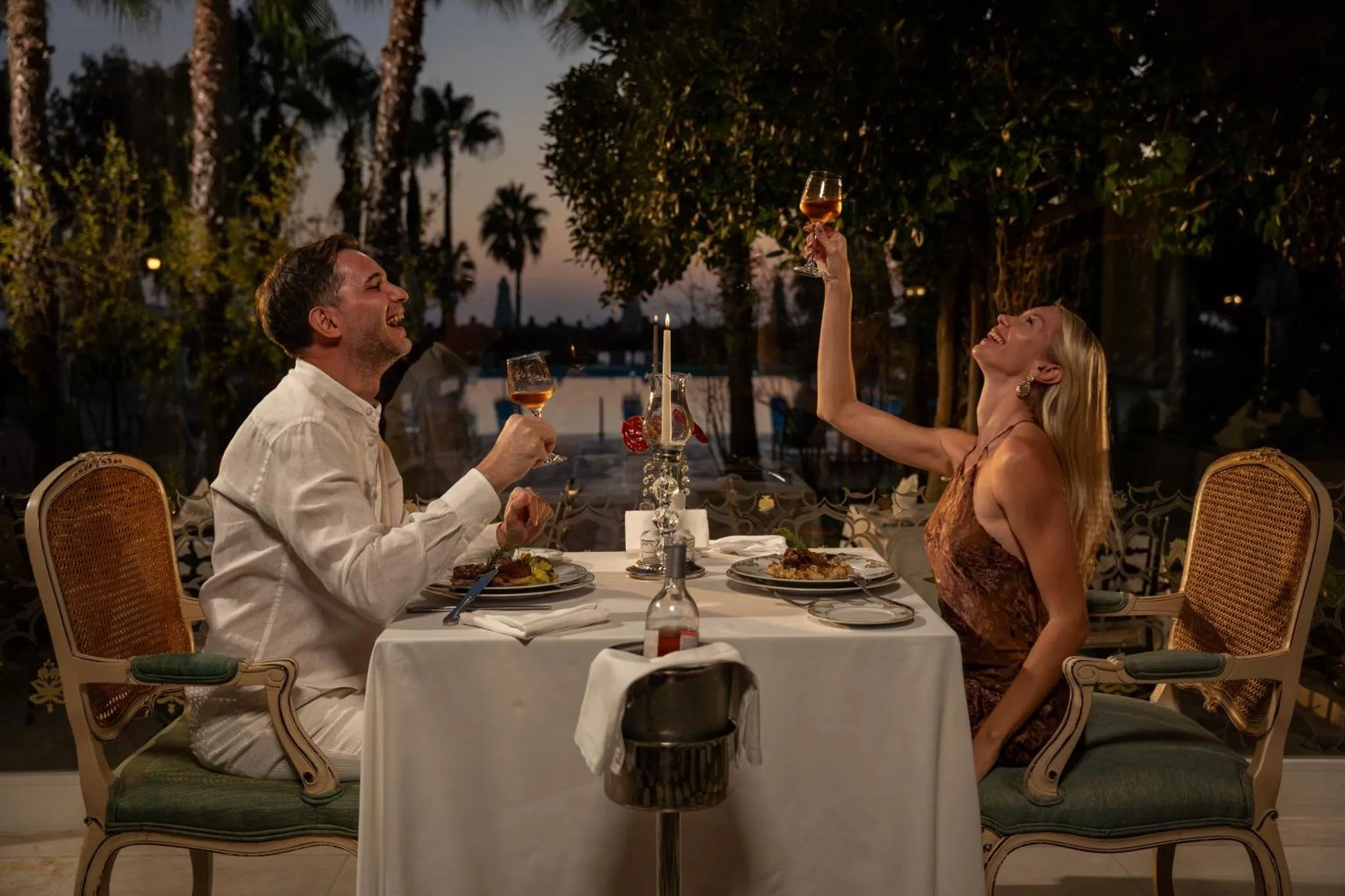 Un couple rit en levant ses verres lors d'un dîner en extérieur.