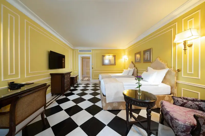 Chambre lumineuse avec deux lits et un sol à carreaux noir et blanc.