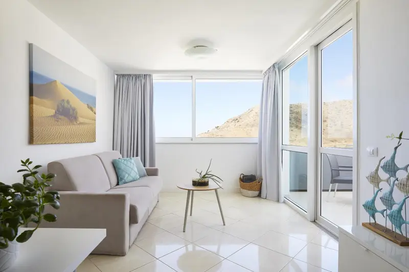 Un salon clair avec un canapé et une vue sur un paysage désertique.