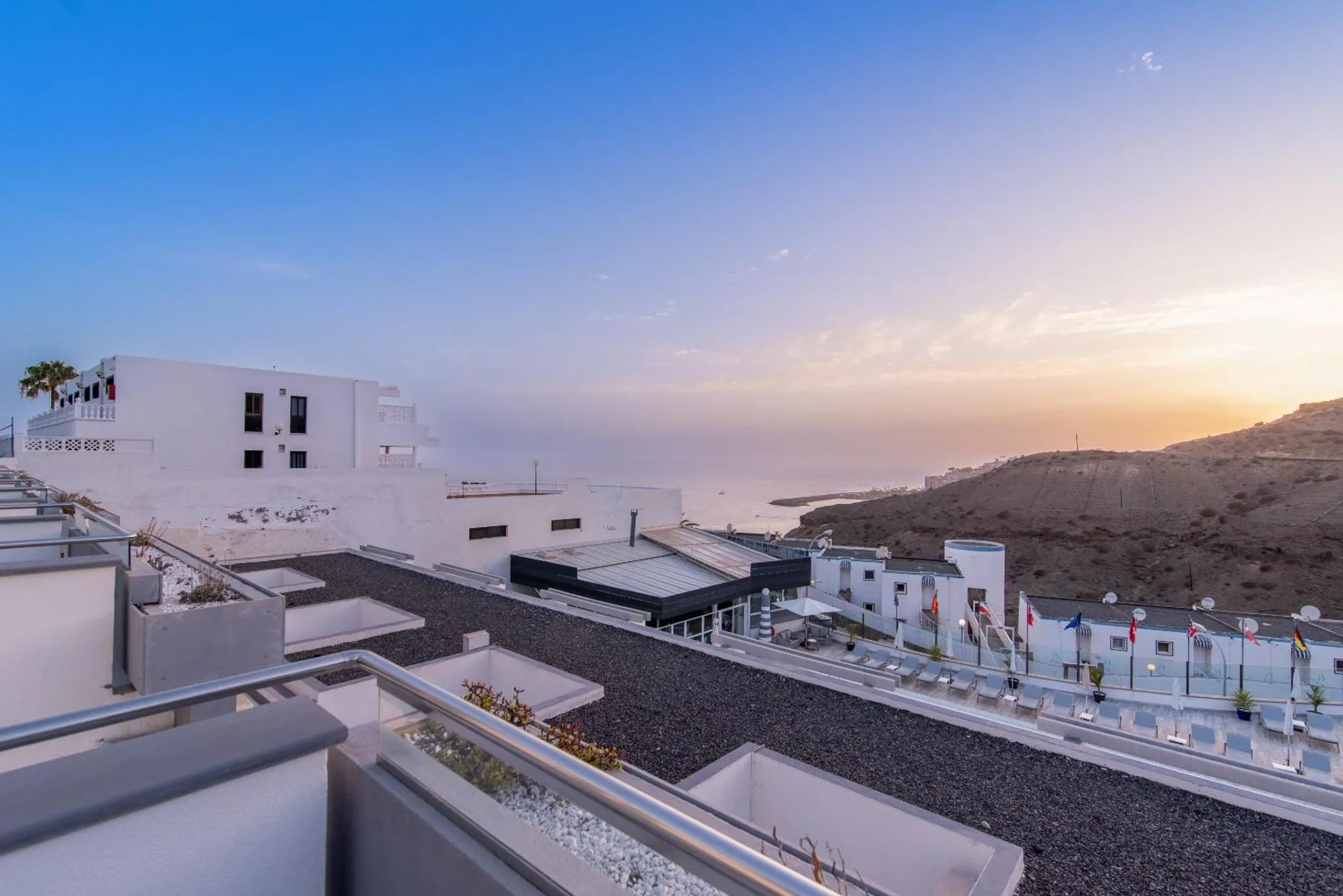 Terrasse avec transats et vue sur la mer au coucher du soleil.