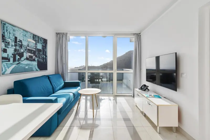 Un salon lumineux avec canapé bleu et vue sur un paysage montagneux.