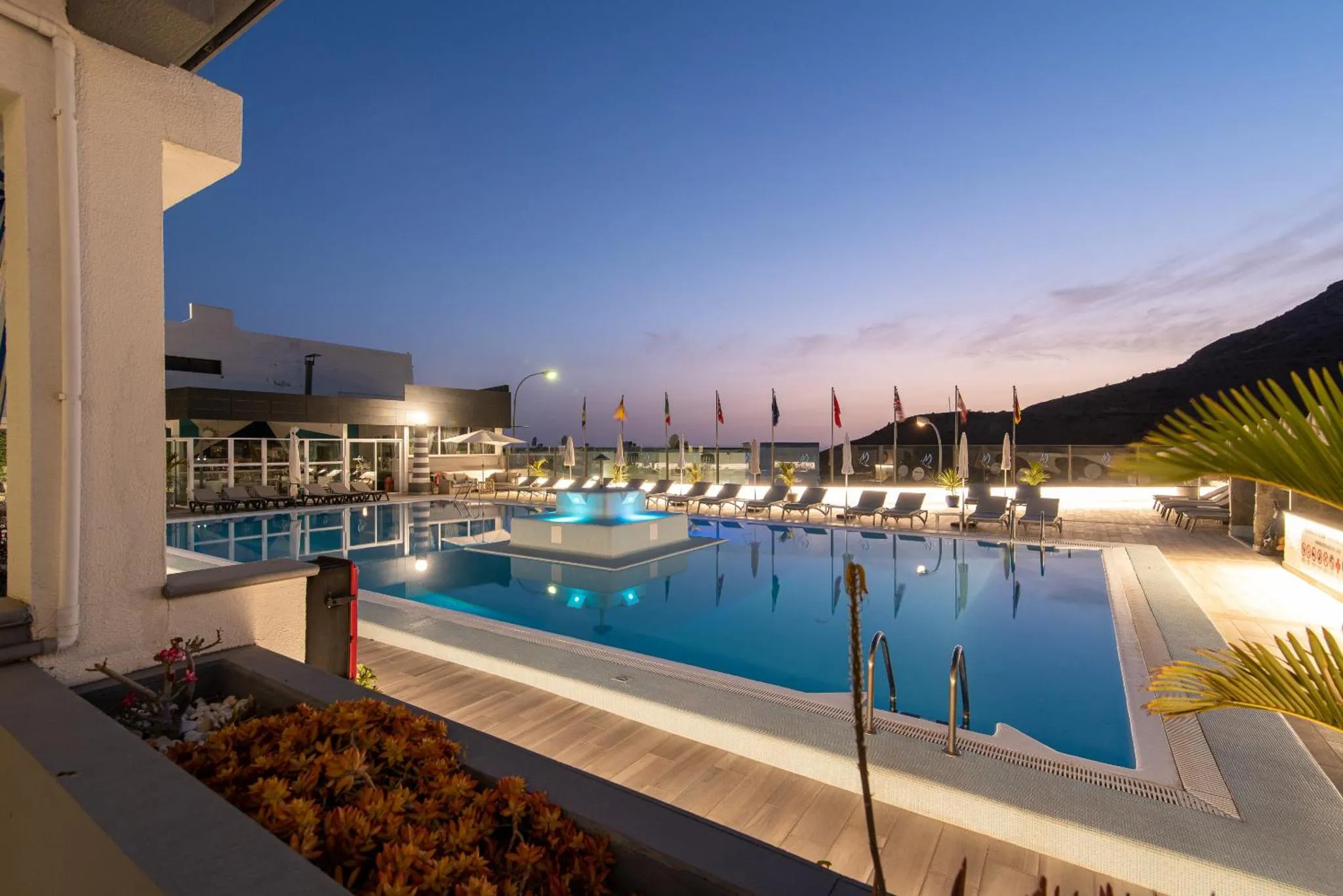Une piscine illuminée au crépuscule avec des transats et des parasols.