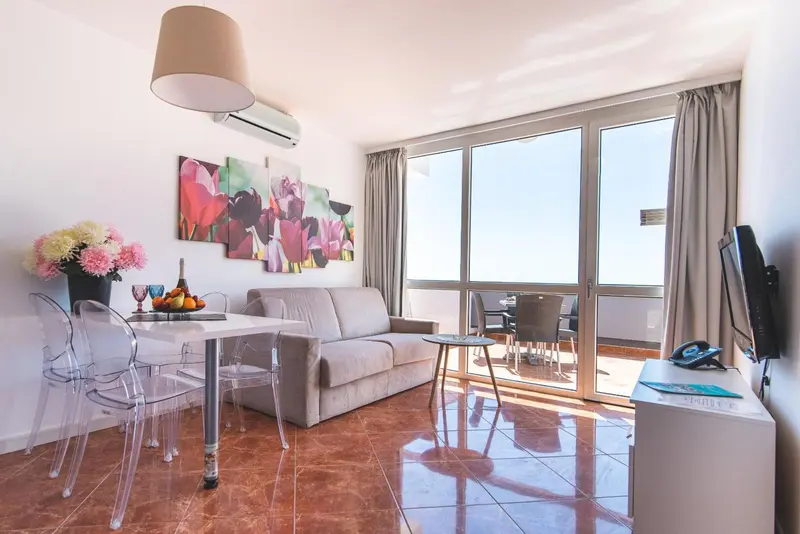 Espace de vie lumineux avec canapé, table et accès à un balcon.