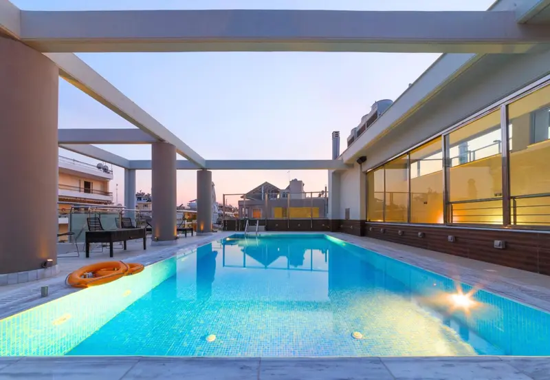 Une piscine rectangulaire avec des transats sur une terrasse en soirée.