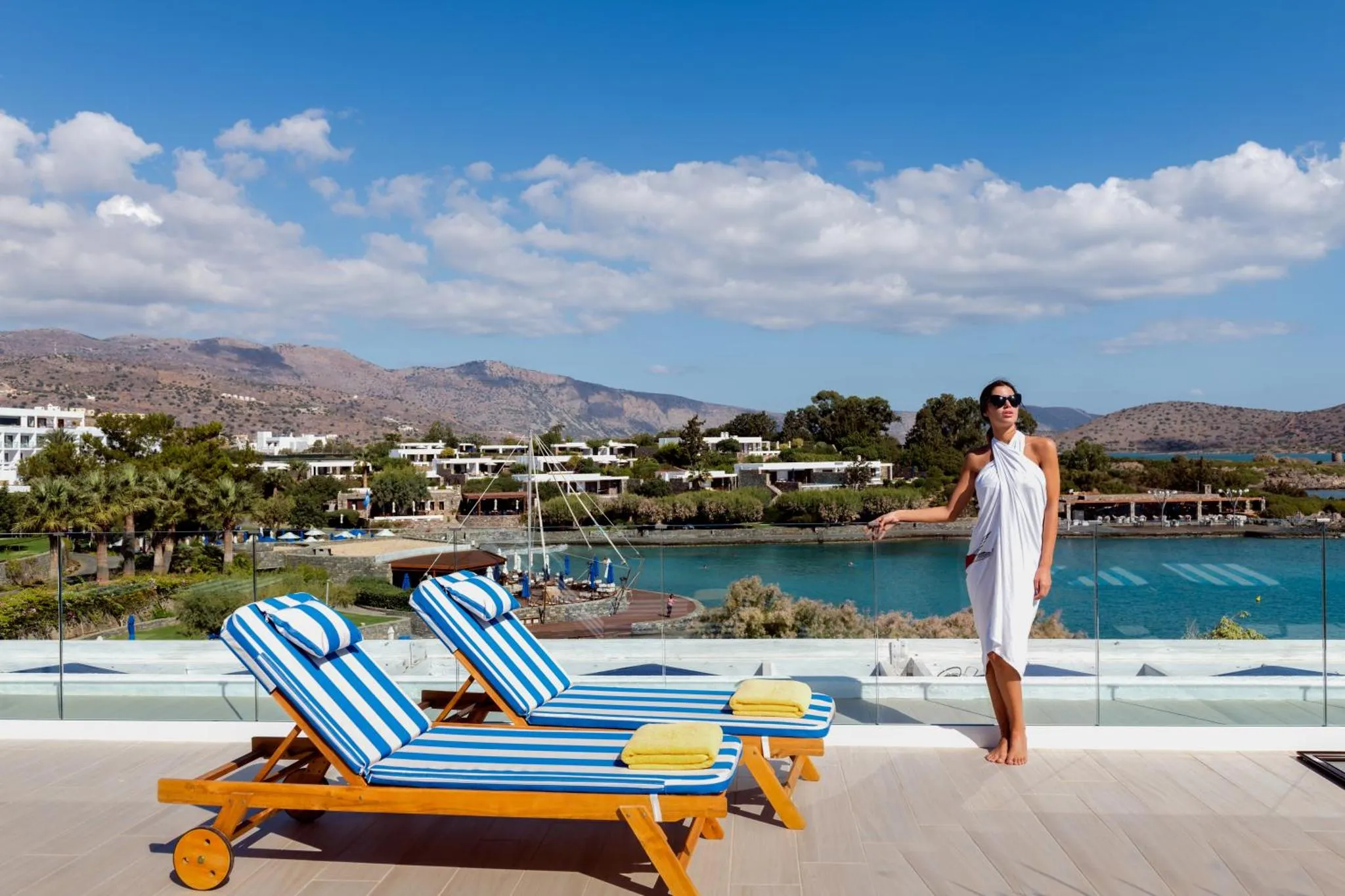 Une femme se tient sur une terrasse avec vue sur la mer et les montagnes.