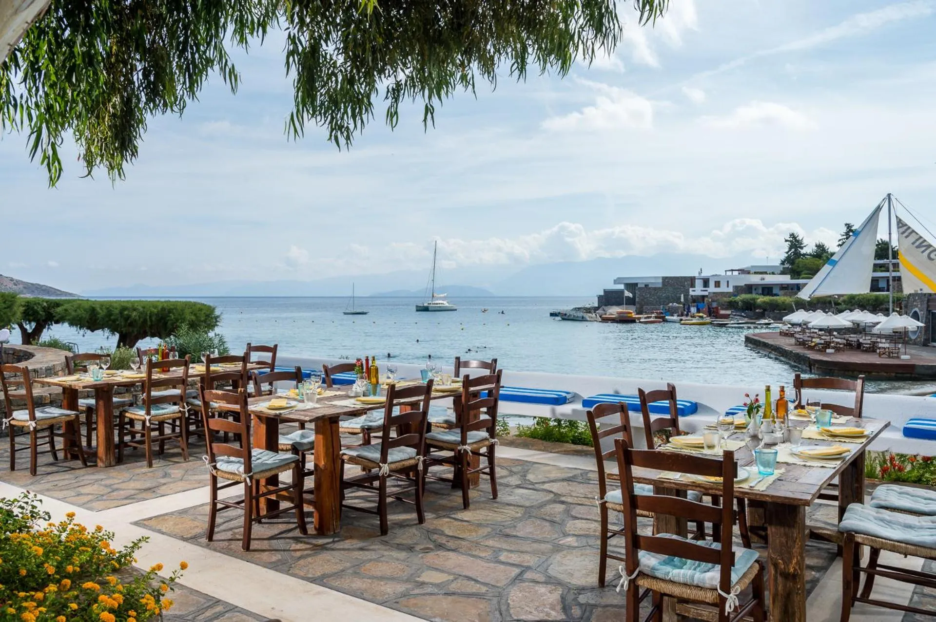 Tables de restaurant en terrasse avec vue sur la mer et des bateaux.