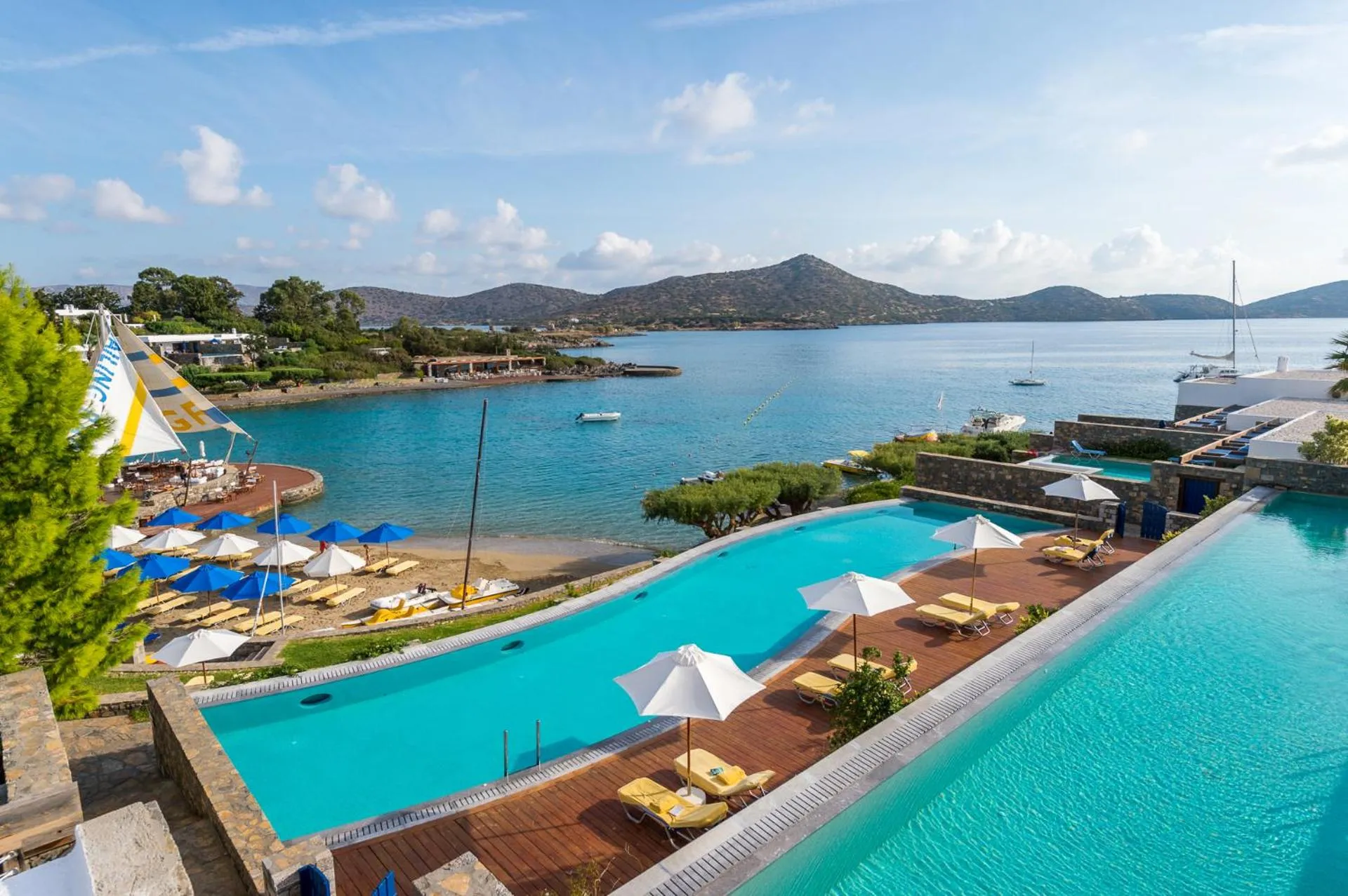 Piscine turquoise avec transats et parasols, vue sur la mer et les collines.