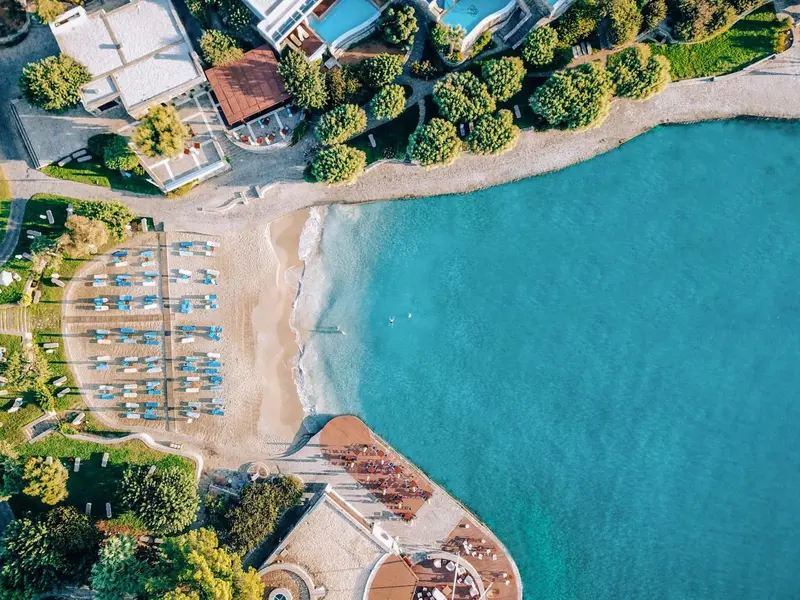 Vue aérienne d'une plage de sable fin bordée d'une eau turquoise et d'une végétation luxuriante.