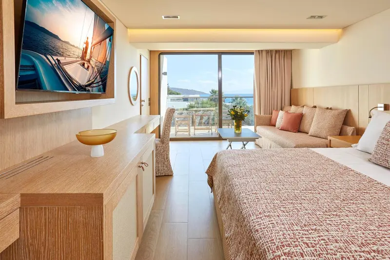 Une chambre lumineuse avec un grand lit et un canapé face à une baie vitrée.