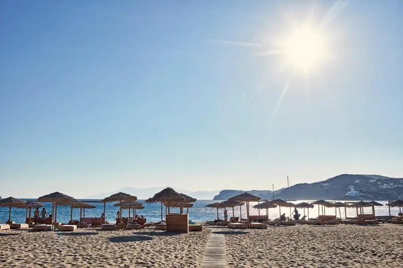 Transats et parasols sur une plage de sable fin, avec une mer turquoise à l'horizon.