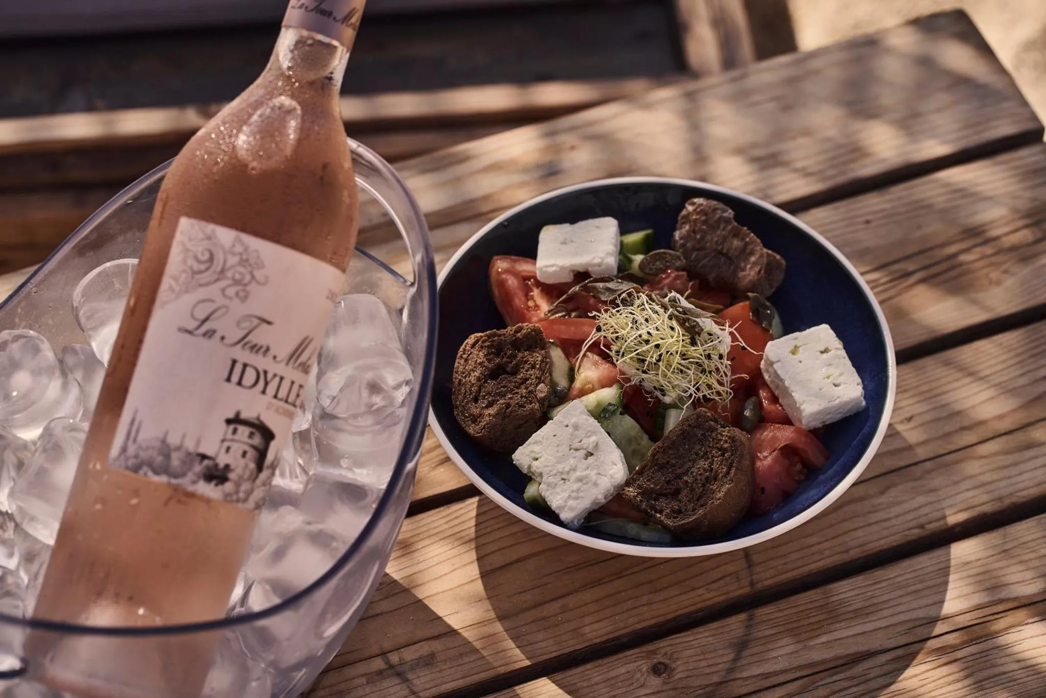 Une salade grecque et une bouteille de rosé rafraîchissent une table en bois.